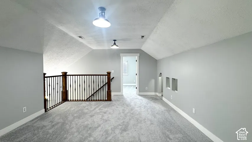 Carpeted upper-level landing featuring a wrought iron and wood banister, sloped ceilings, and recessed wall cutouts
