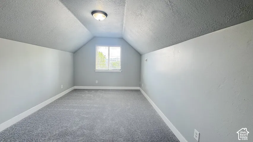 Bedroom with new carpet, featuring vaulted ceilings and neutral gray walls and white baseboards.