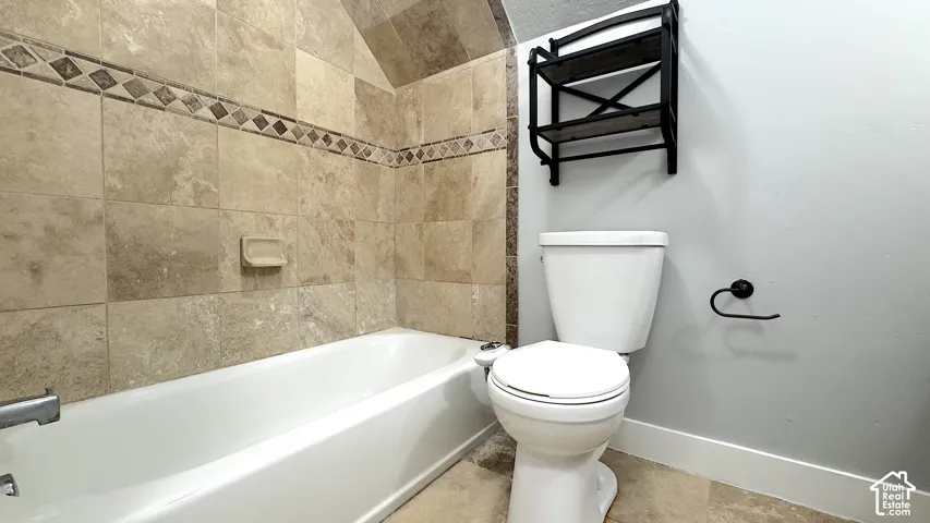 Upstairs hallway bathroom featuring a white tub, tile stone-finished walls with a decorative accent band, and a white toilet.