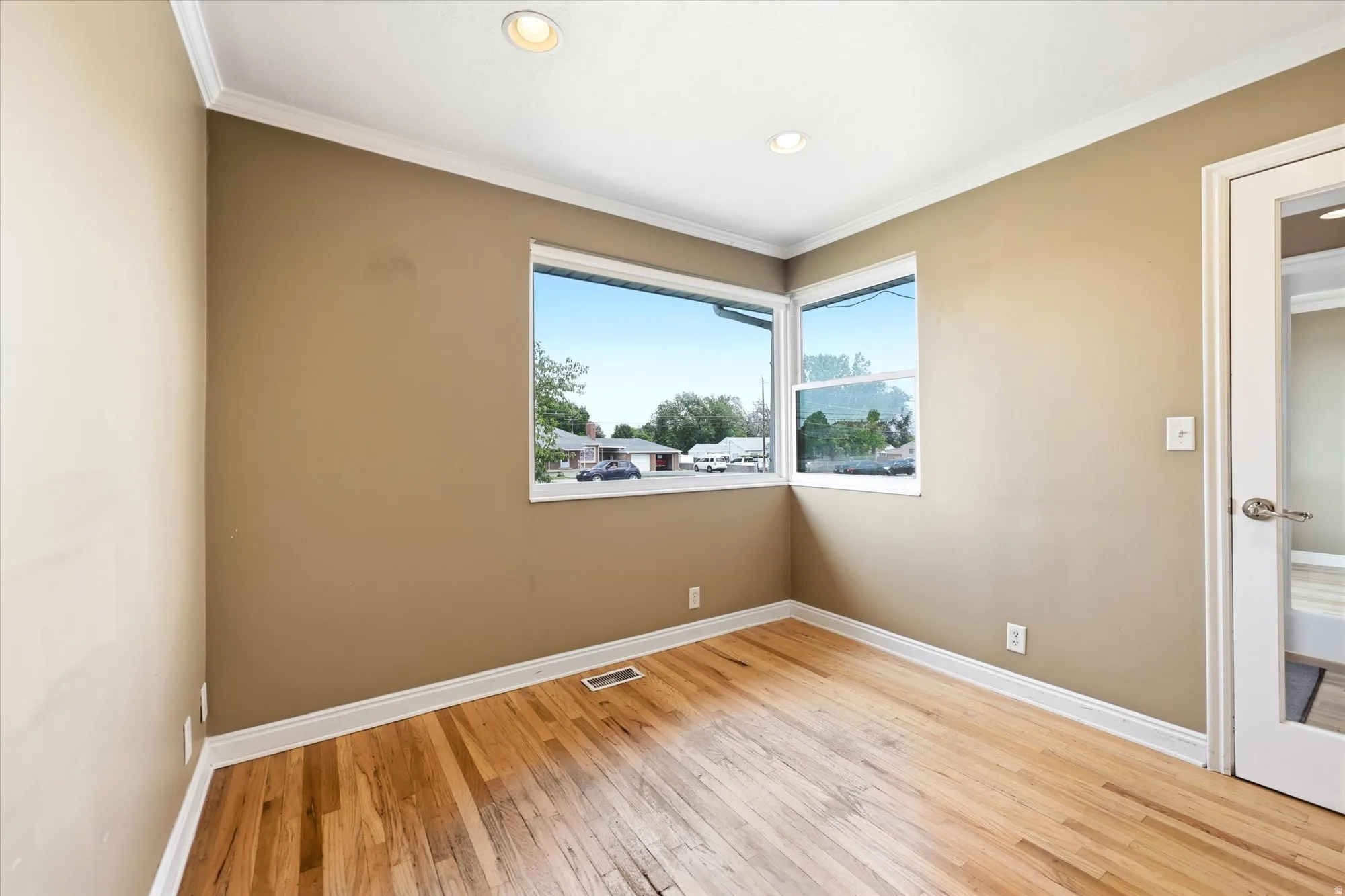 Hardwood flooring throughout, complemented by two windows, recessed lighting, and white crown molding