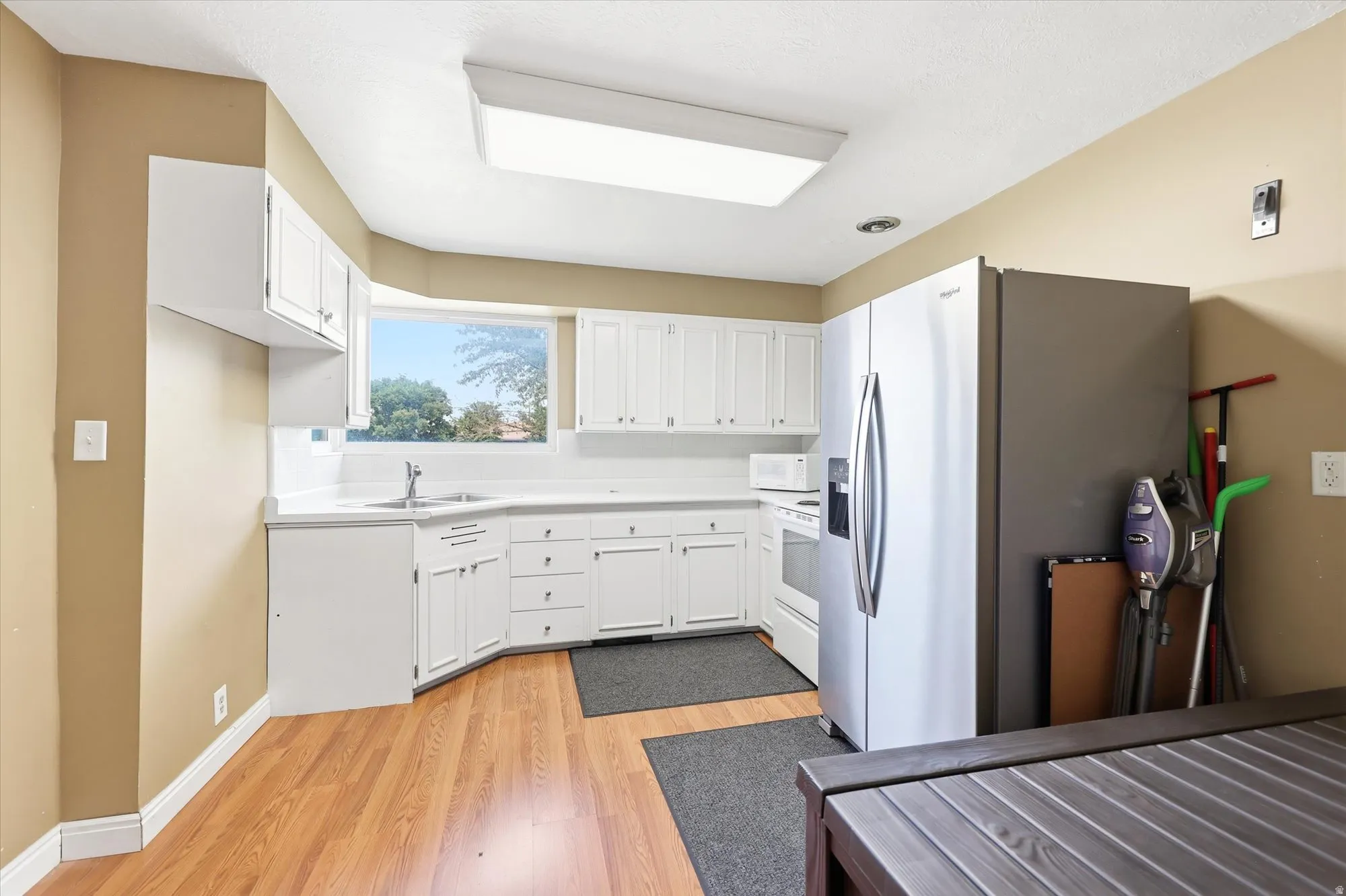 Full kitchen featuring wood-finish flooring, white cabinetry, white countertops, built-in appliances, and a window above the sink