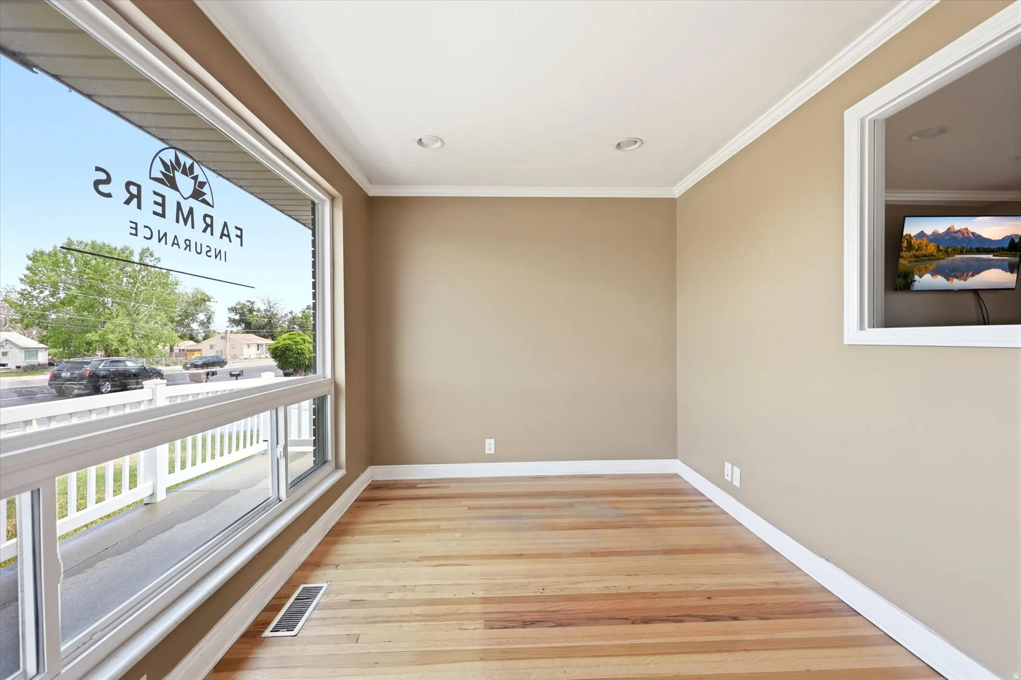 Spacious room featuring broad plank wood flooring, neutral wall tones, crisp white crown molding, and recessed lighting