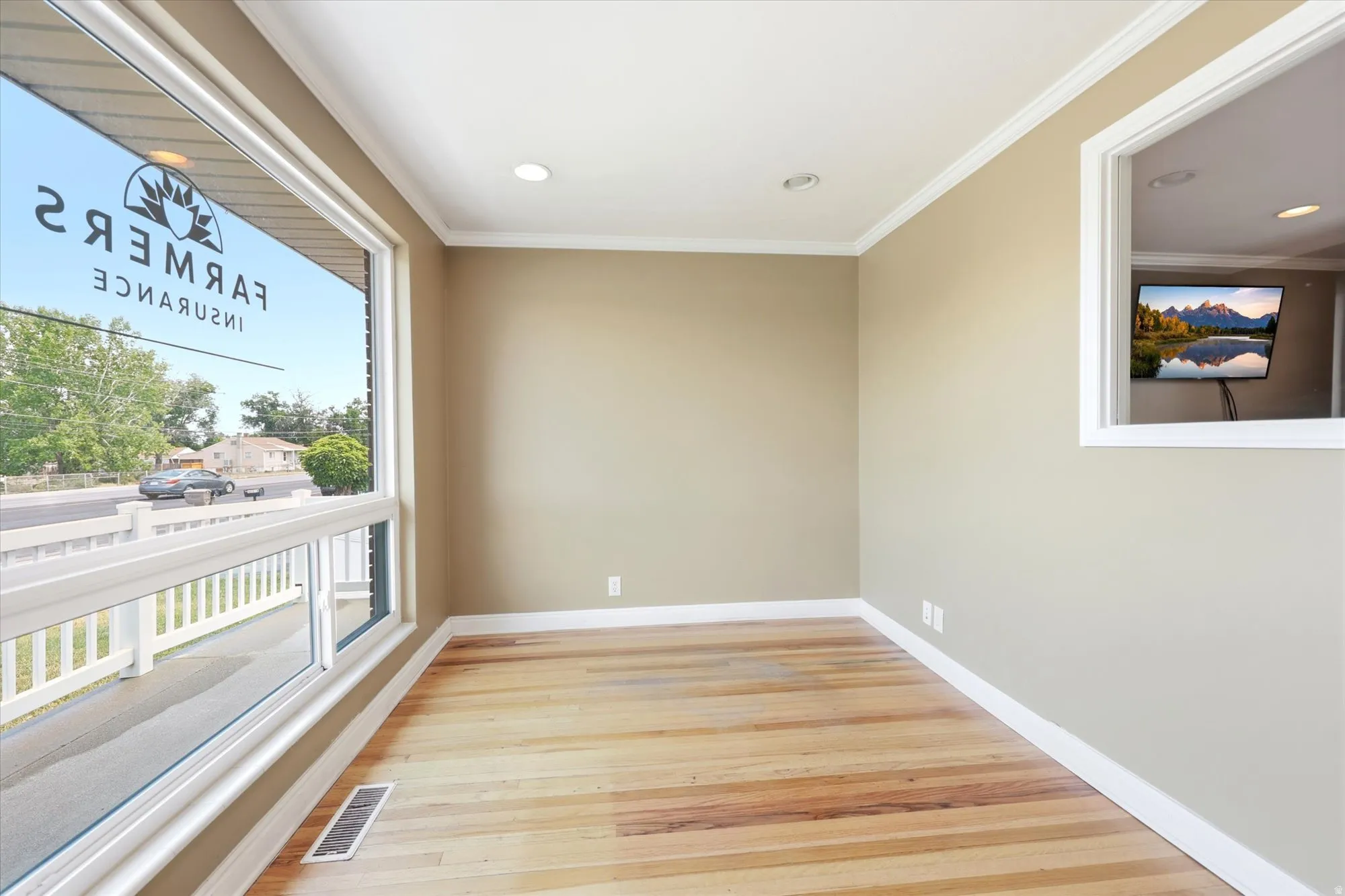 Spacious room featuring wide plank wood flooring, recessed lighting, crown molding, and large picture windows