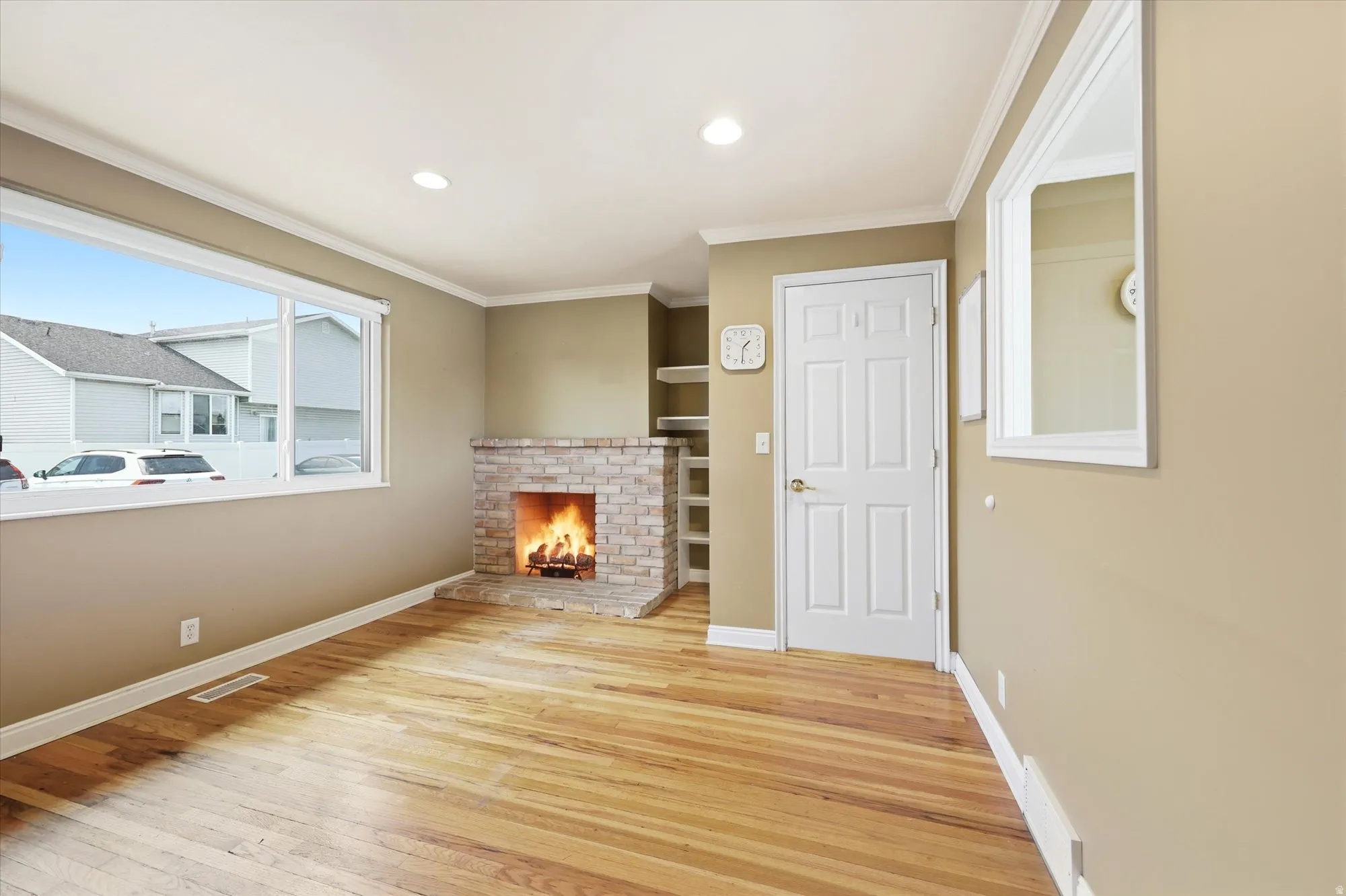 Living area featuring wood-finish flooring, a brick fireplace, built-in shelving, a large picture window, and recessed lighting