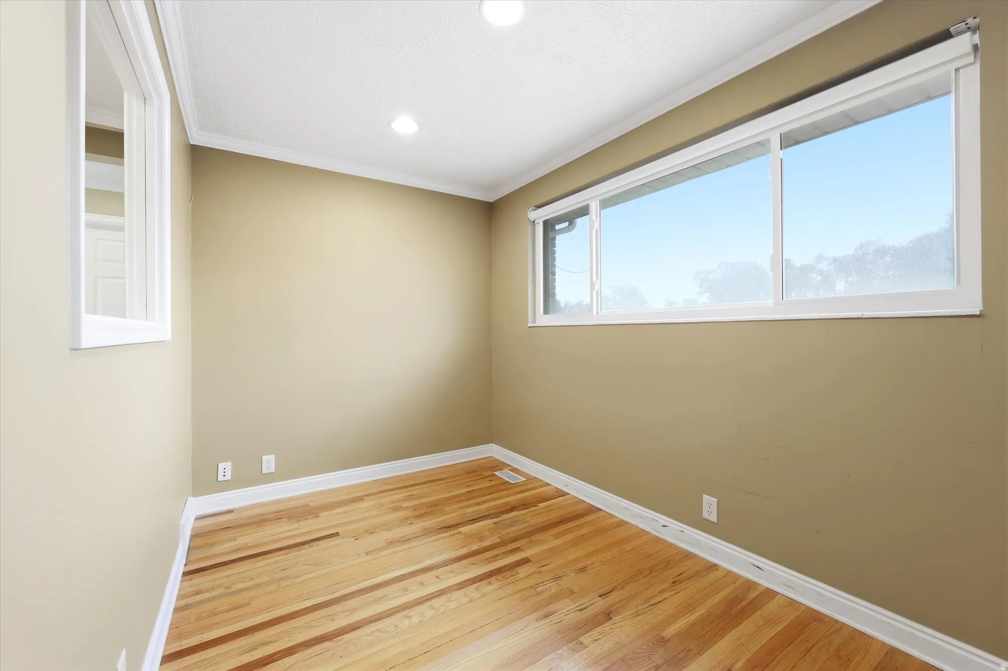 Hardwood flooring complemented by a wide window, recessed lighting, and crown molding