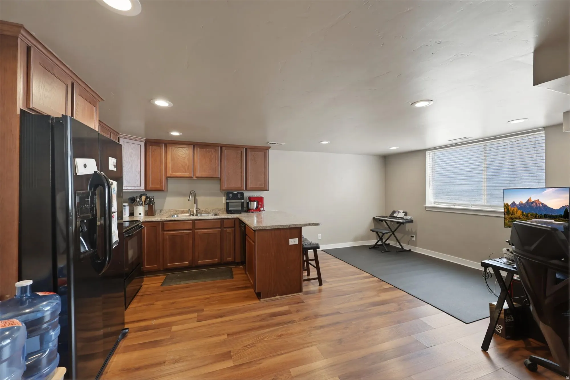 Kitchenette featuring medium-toned wood cabinetry, stone countertops, and a black appliance suite
