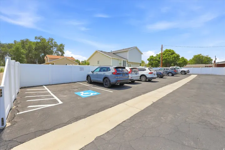 Paved parking area featuring multiple designated parking spaces, a white privacy fence, and a marked accessible parking space