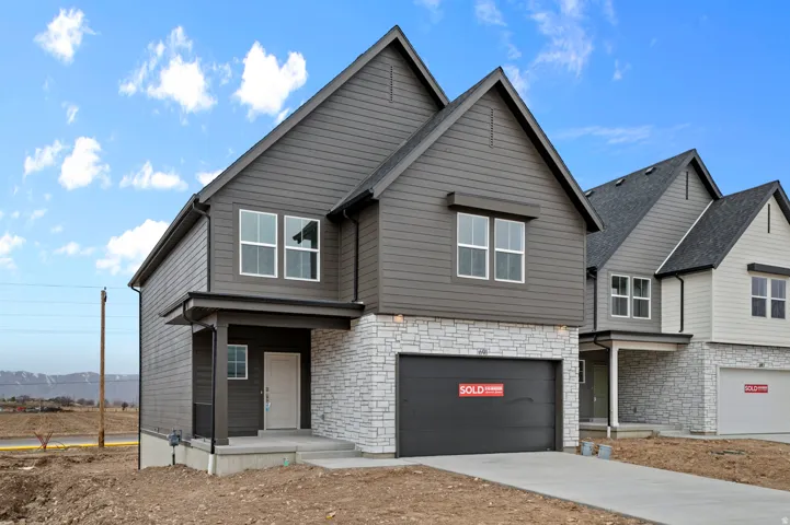 Modern two-story home featuring a dark gray exterior with stone accents, a two-car garage, and a covered entryway