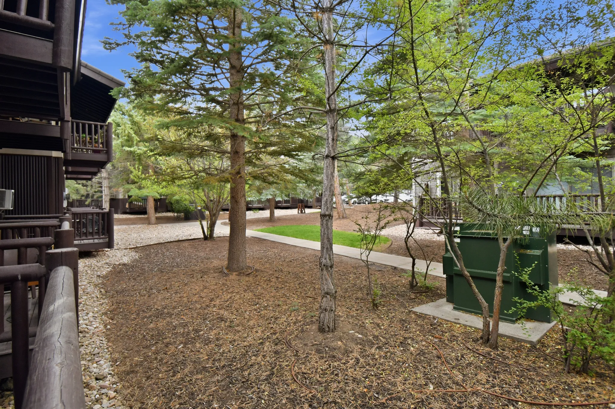 Wood-sided building with multiple balconies featuring wood railings and mature evergreen trees