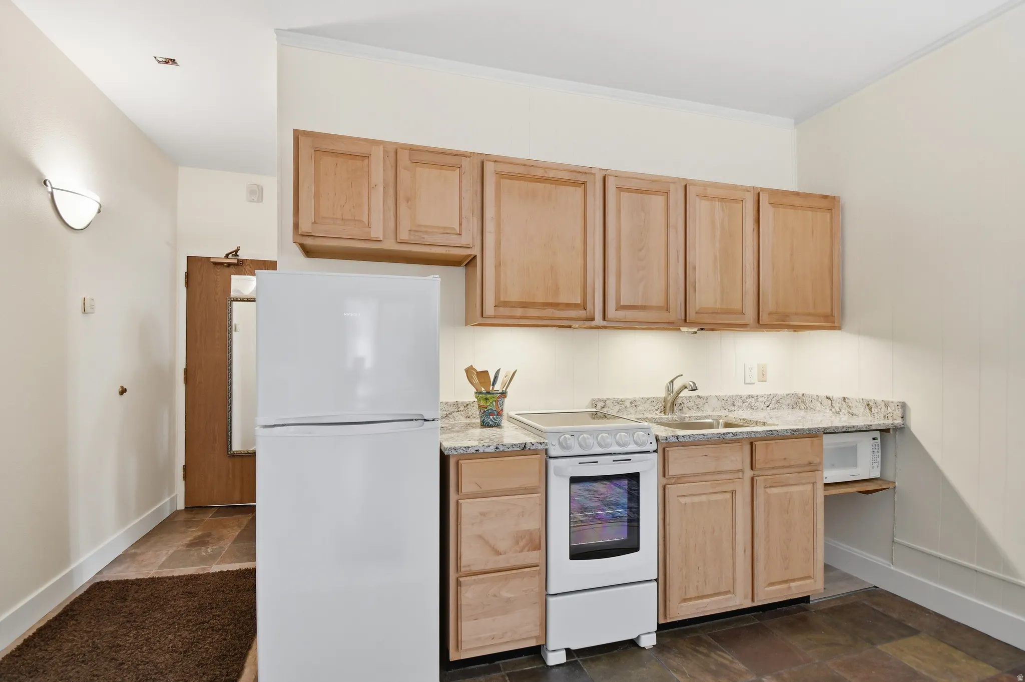 Compact kitchen featuring light wood-finish cabinetry, granite-style countertops, and a full suite of white appliances