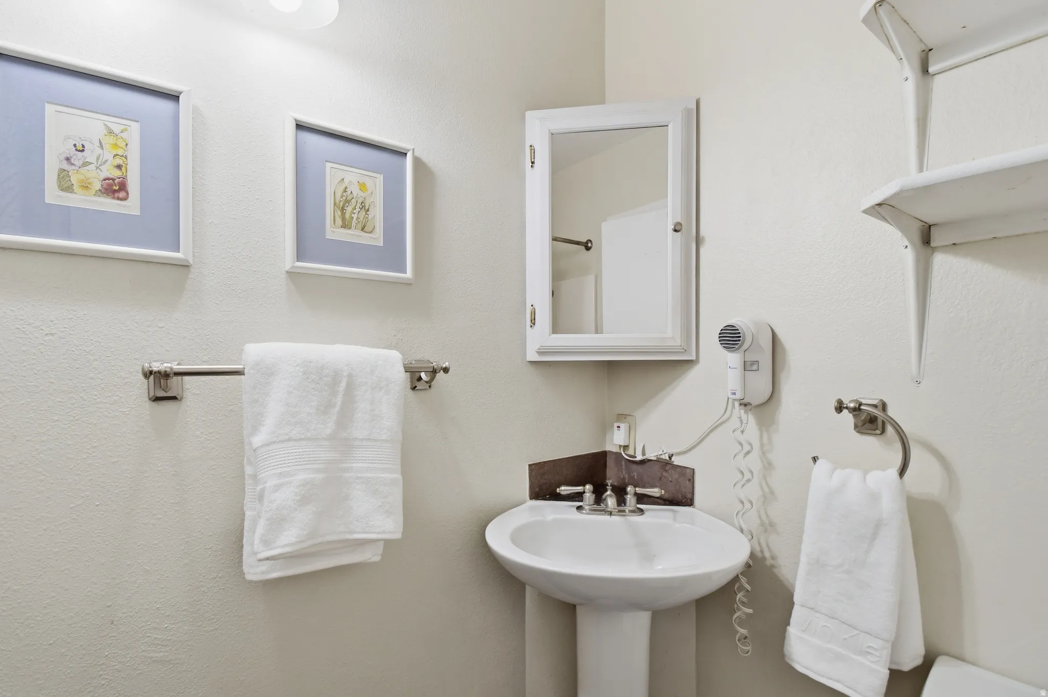 Pedestal sink with chrome-finish fixtures, wall-mounted medicine cabinet, and open shelving