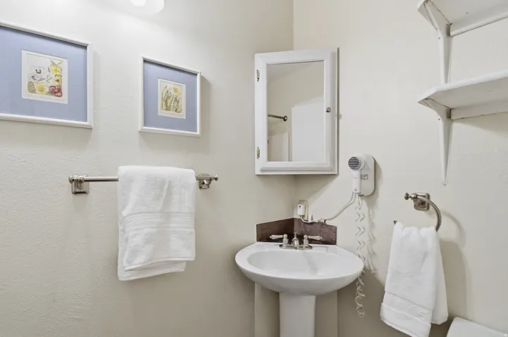 Pedestal sink with chrome-finish fixtures, wall-mounted medicine cabinet, and open shelving