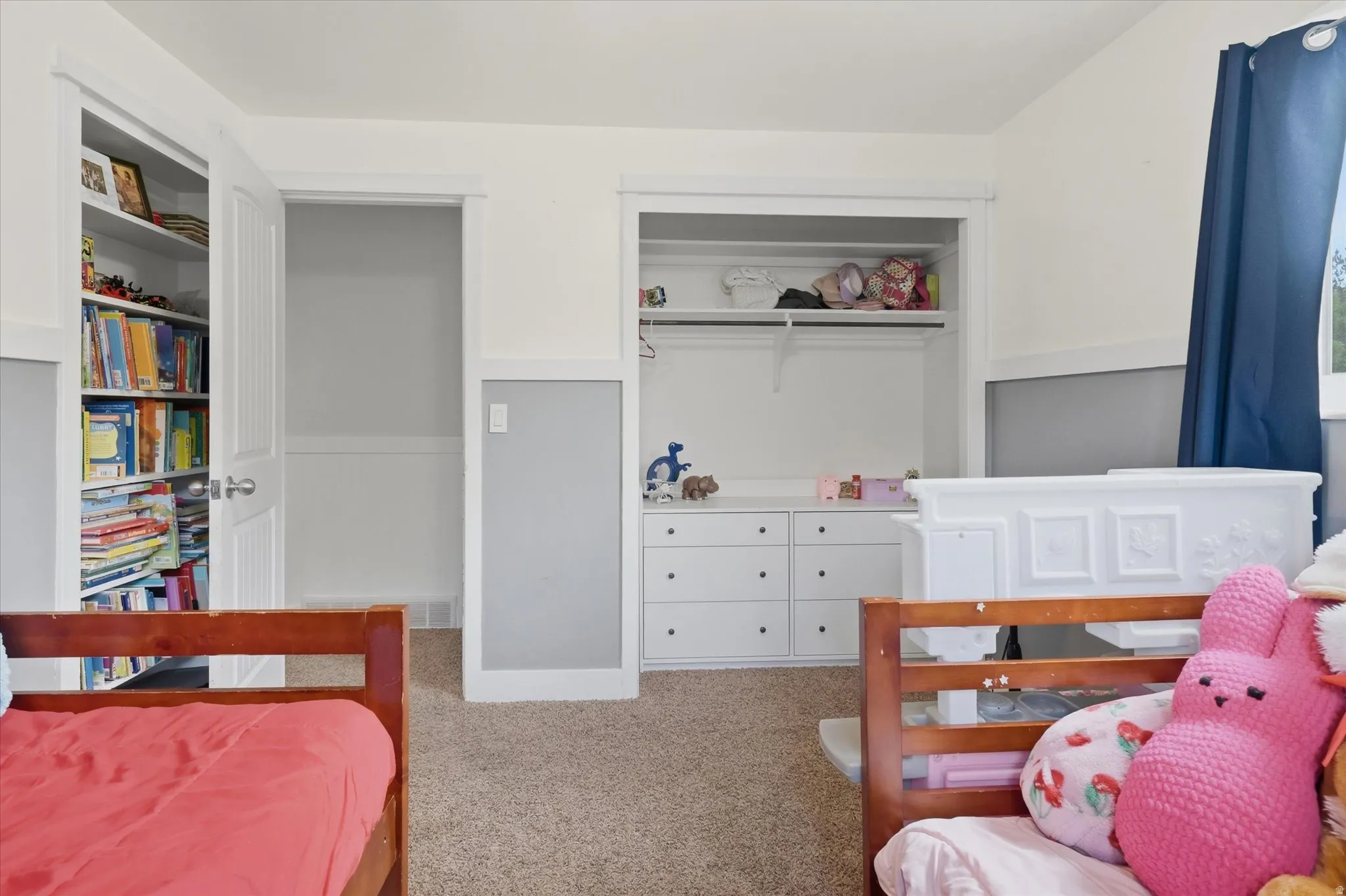 Carpeted room featuring a built-in bookshelf, white trim, and a window with blue curtains
