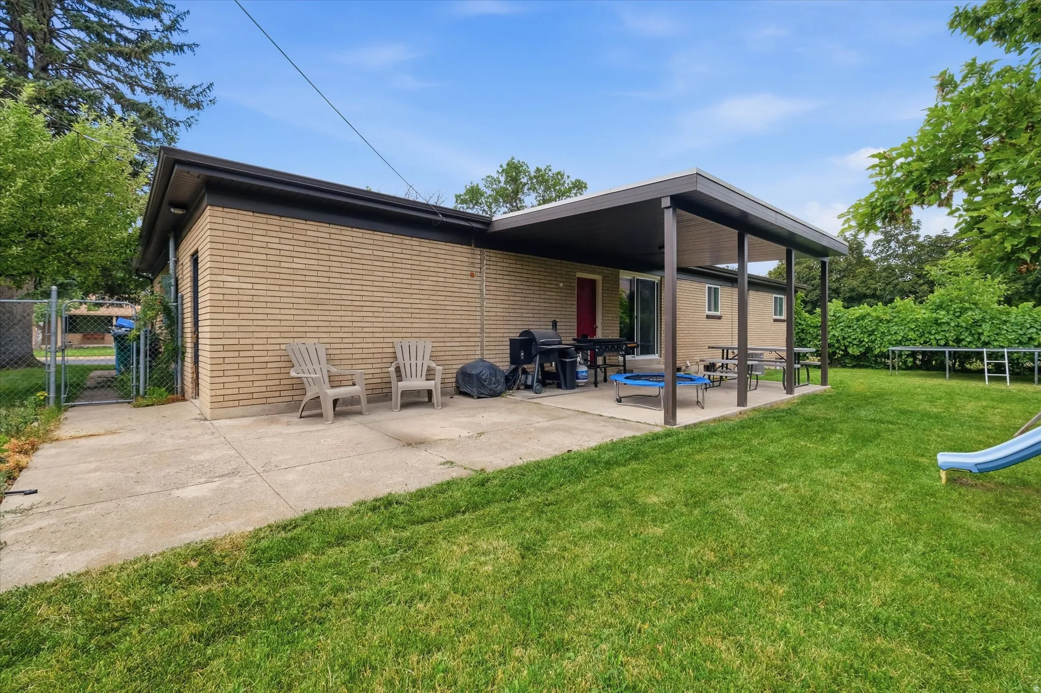 Rear exterior featuring a covered patio, expansive lawn, and brick facade