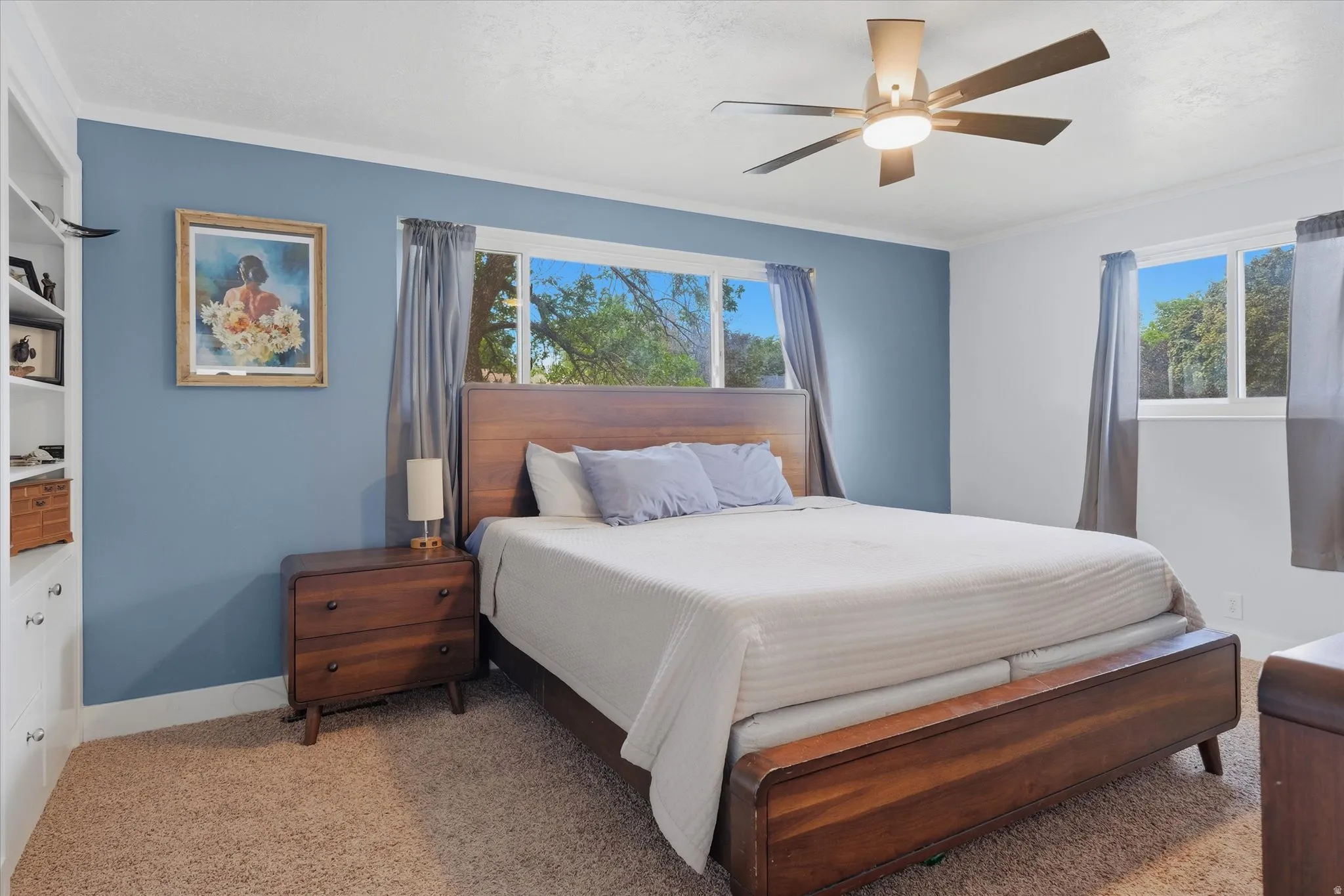 Bedroom featuring a built-in bookshelf, multiple windows, a ceiling fan with integrated lighting, and crown molding