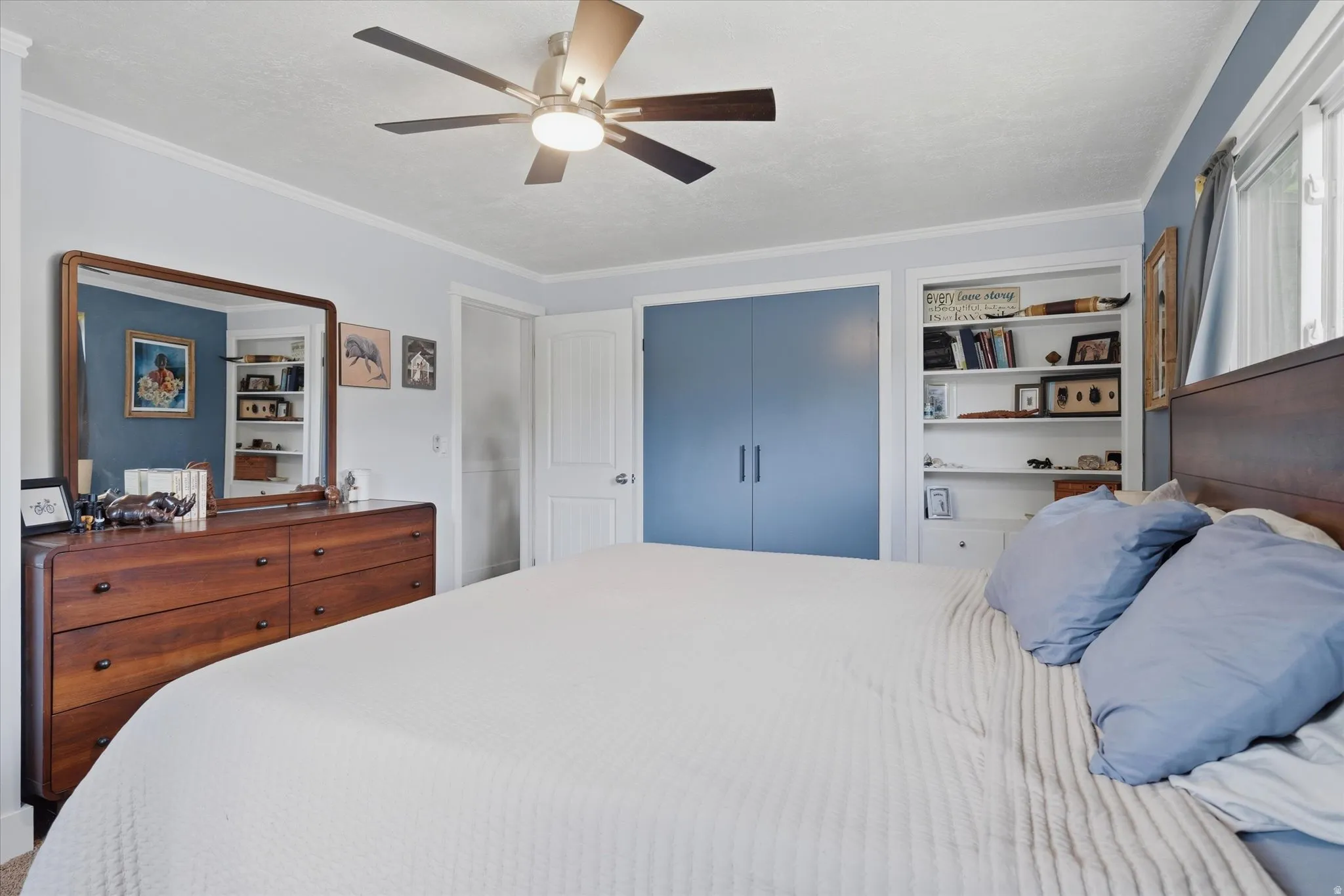 Ceiling fan with integrated lighting, built-in shelving, blue accent wall, and crown molding details