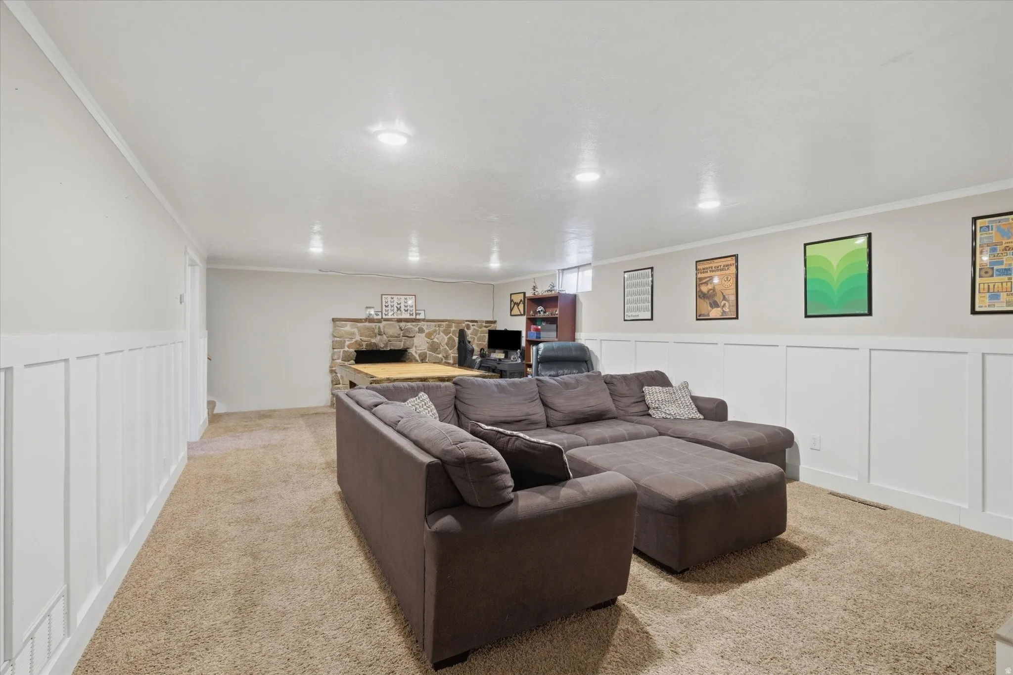 Spacious room featuring light-colored carpeting, white wall paneling, recessed lighting, and a stone-faced bar area