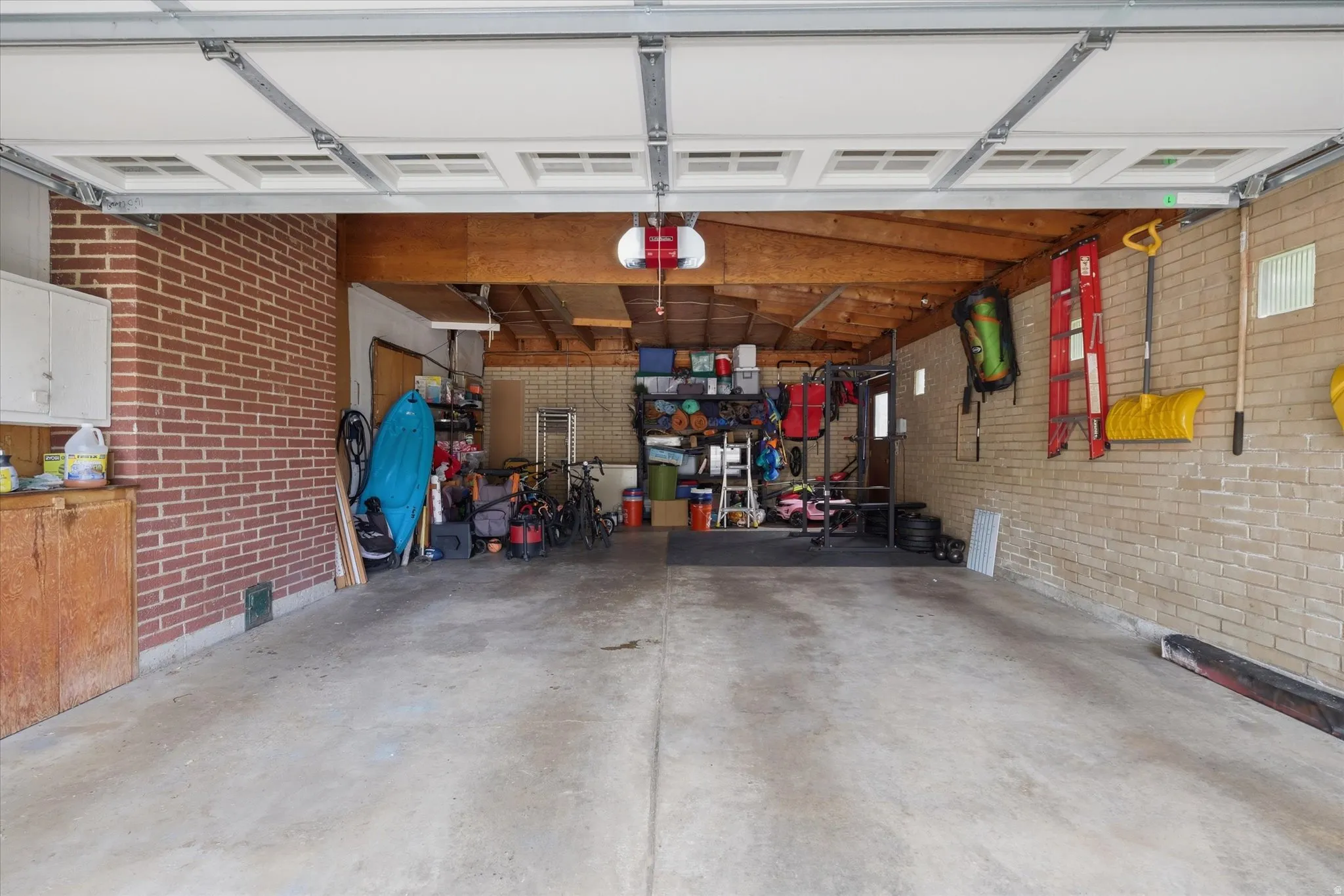 Two-car garage with a concrete floor, exposed wood ceiling beams, and brick walls