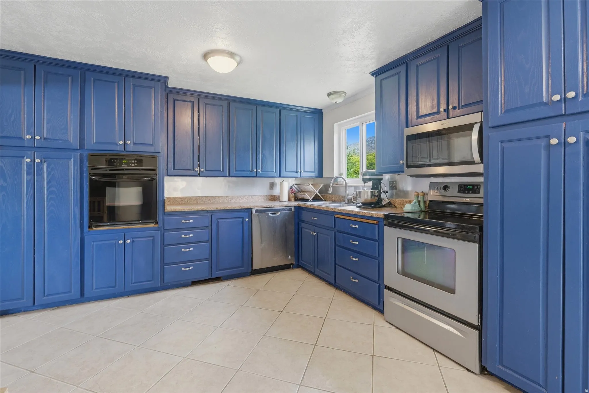 Kitchen featuring extensive blue cabinetry, stainless steel appliances, stone-look countertops, and tile flooring