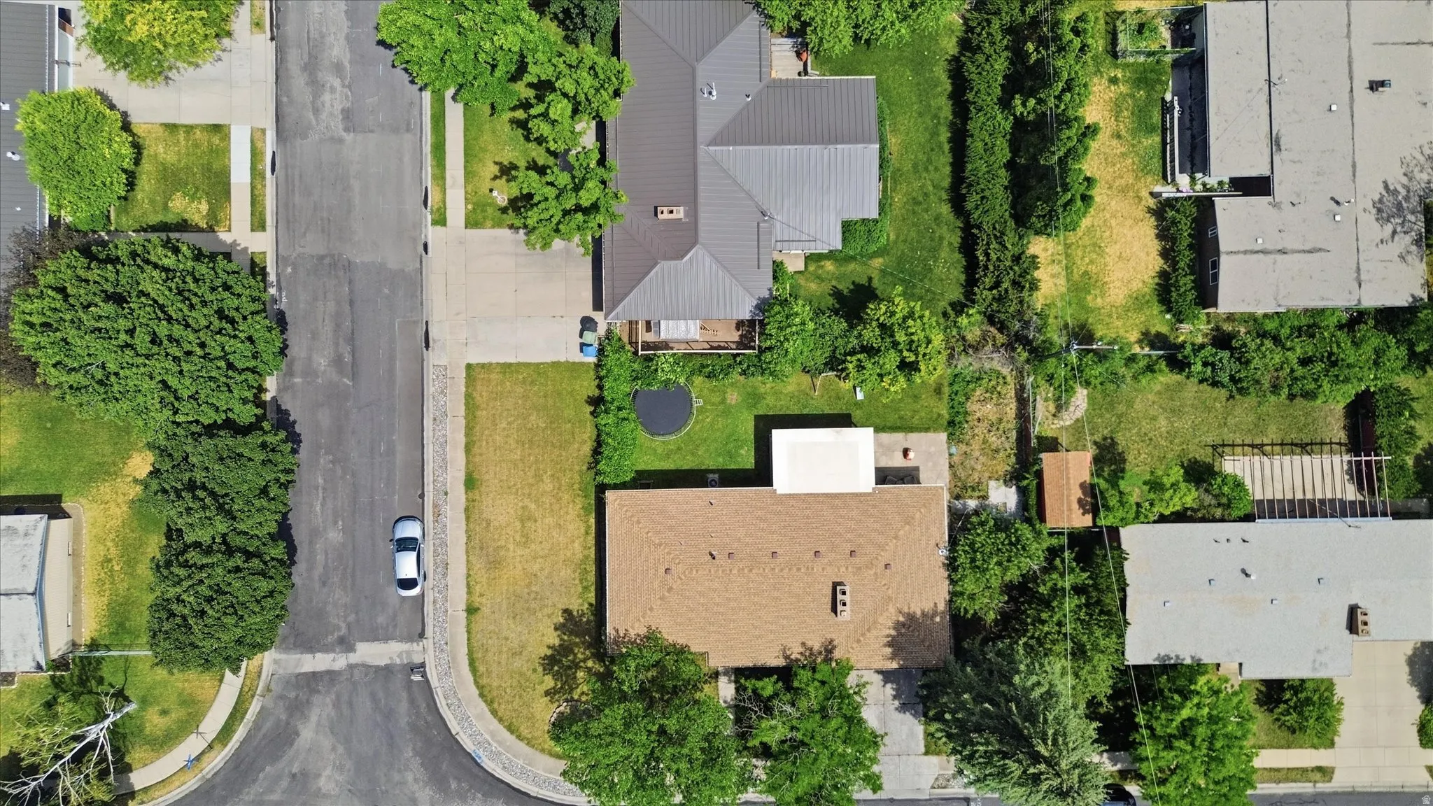 Aerial perspective showcasing a residential property with a brown shingle roof and surrounding green spaces