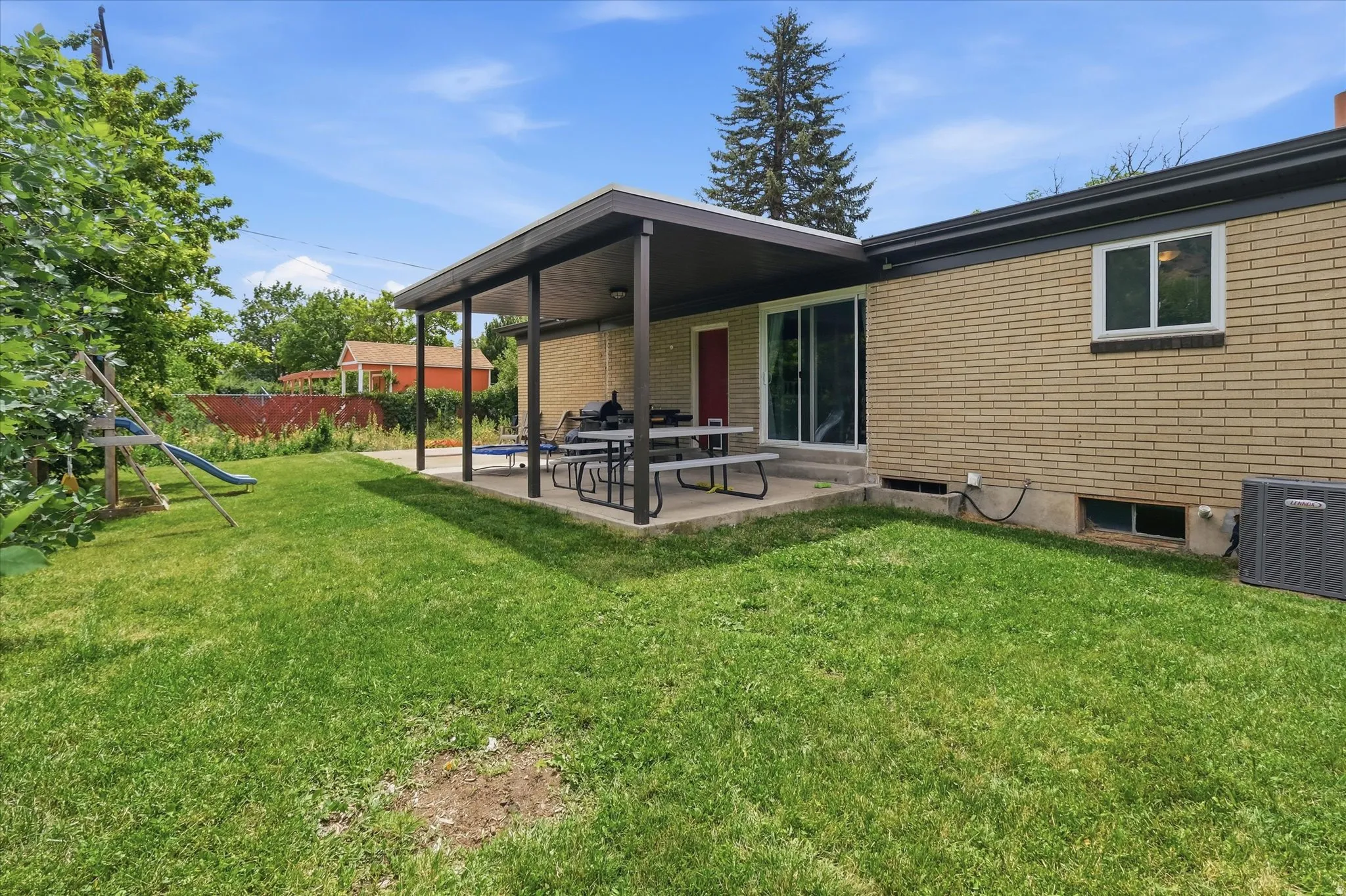 Expansive backyard featuring a covered patio, sliding glass door access, tan brick exterior, and a manicured lawn
