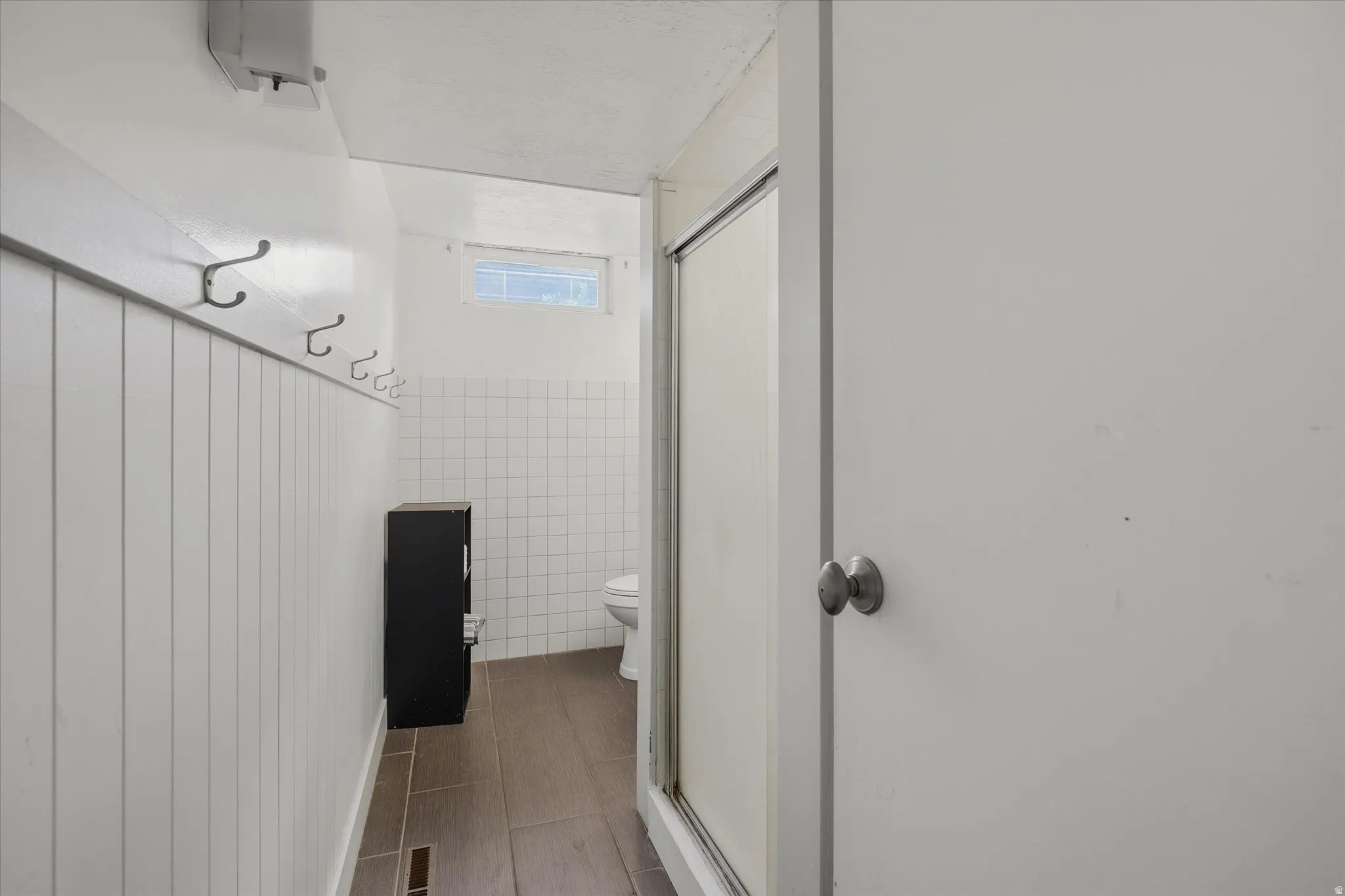 White paneled wall with metal hooks, wood-finish flooring, and white tiled walls