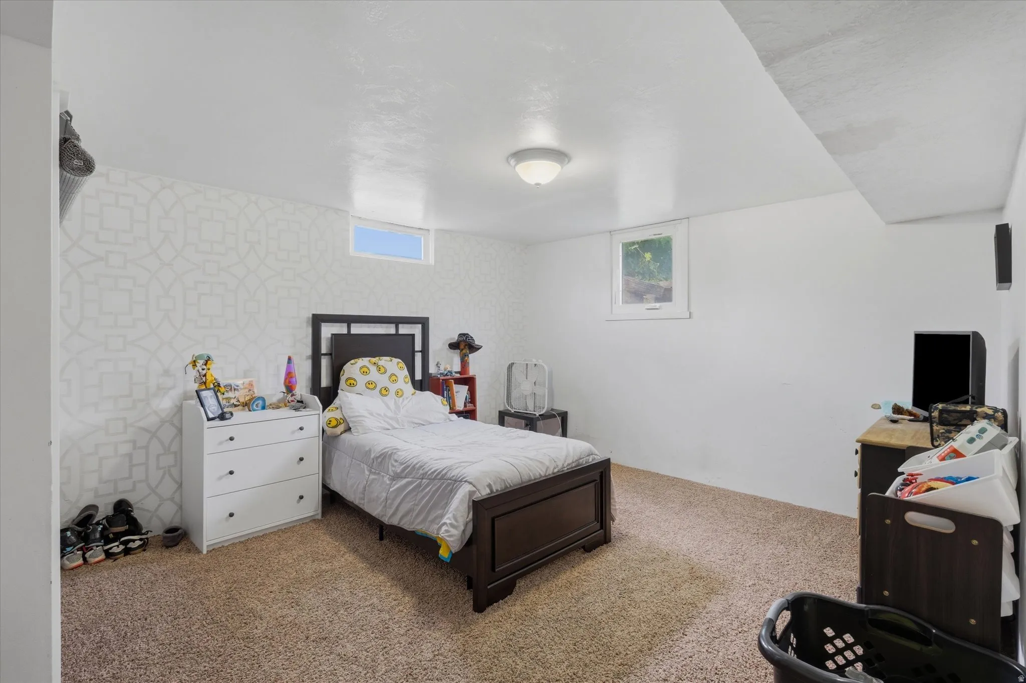 Carpeted room featuring a patterned accent wall, white painted walls, and a white ceiling with a flush-mount light fixture