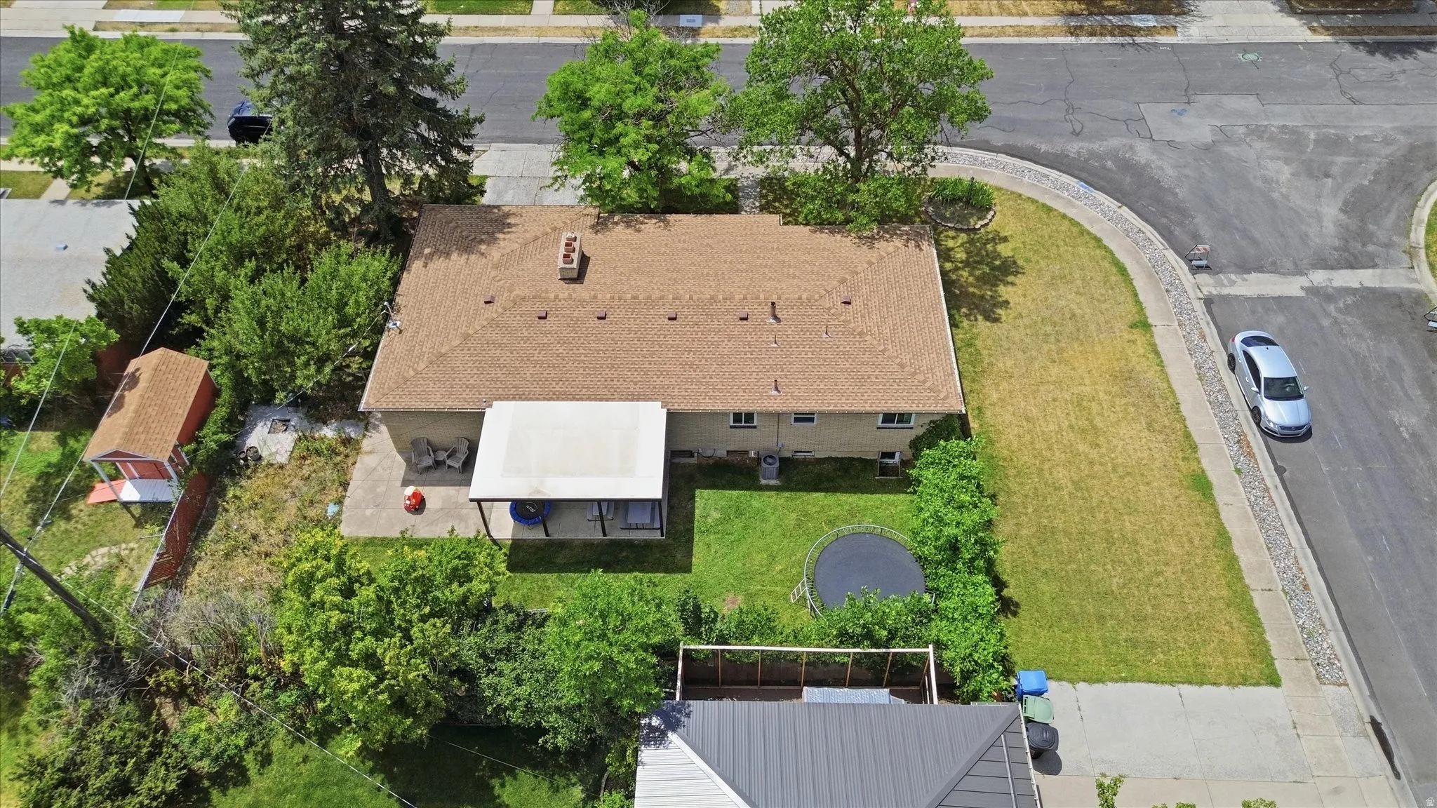 Overhead view of a property featuring a tan-sided residence with a brown shingle roof