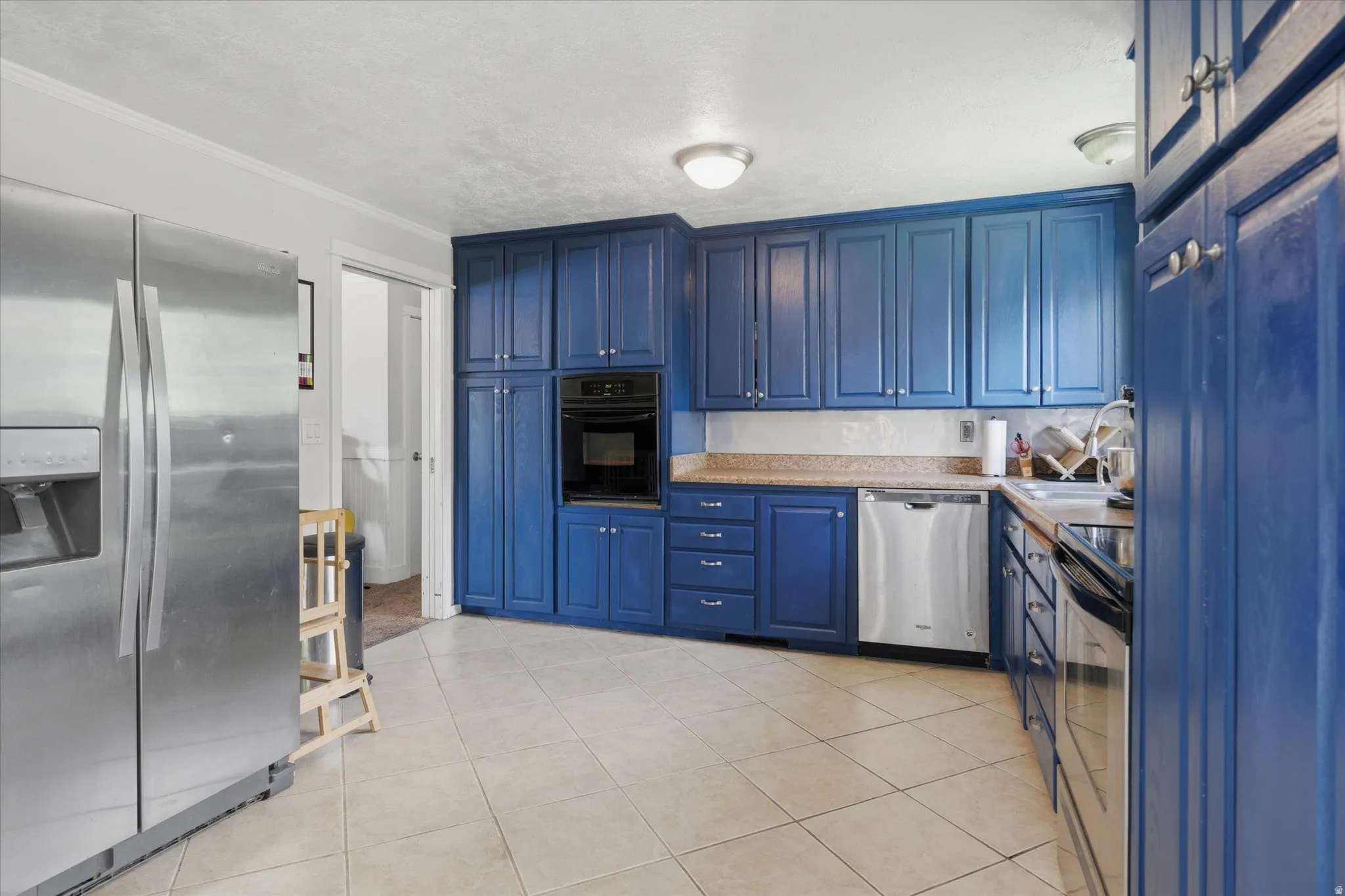 Kitchen featuring custom blue cabinetry, light tile flooring, built-in oven, stainless steel dishwasher, and a stainless steel side-by-side refrigerator