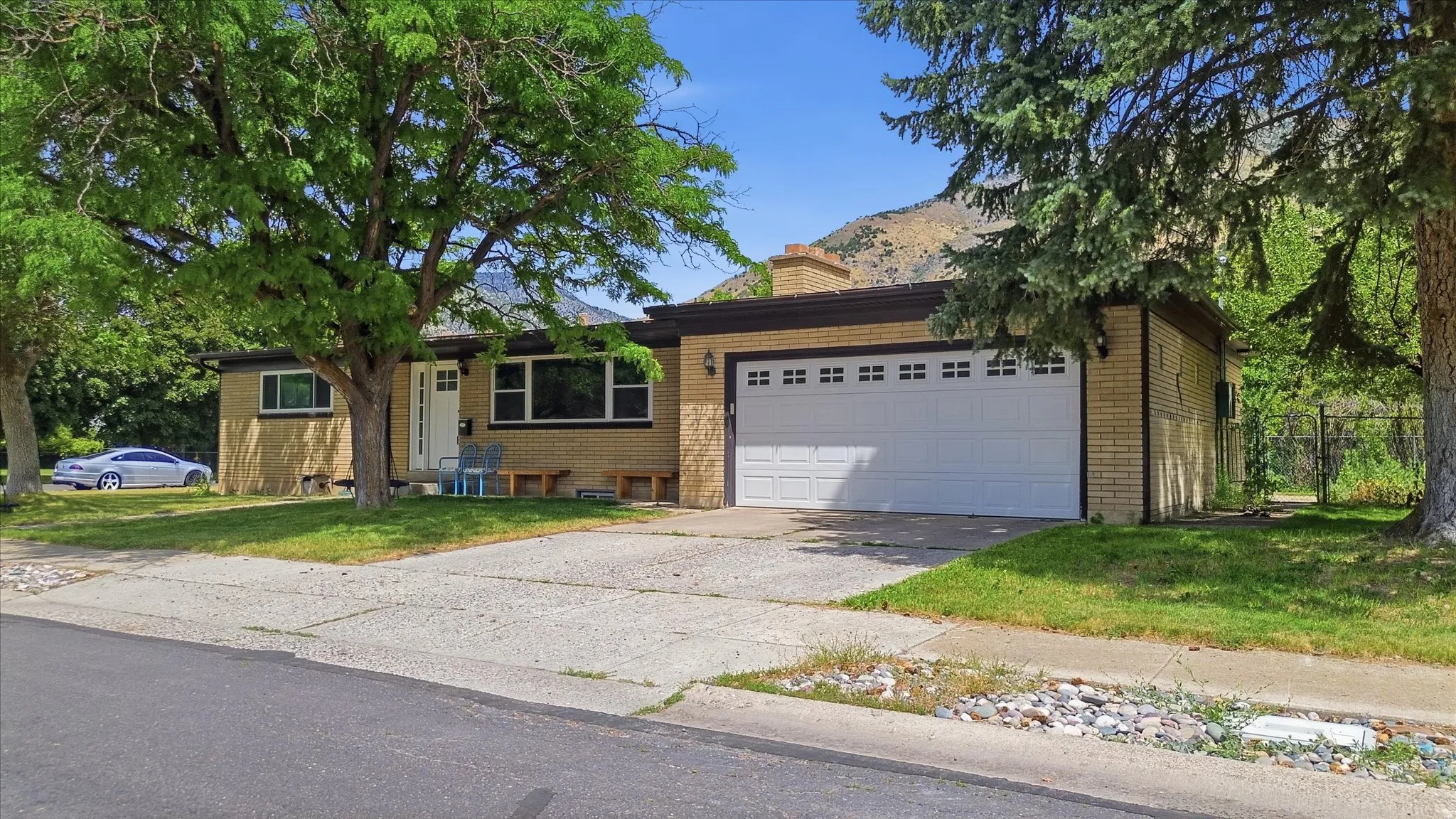 Brick exterior featuring an attached two-car garage, multiple windows, a front entry door, and mature landscaping