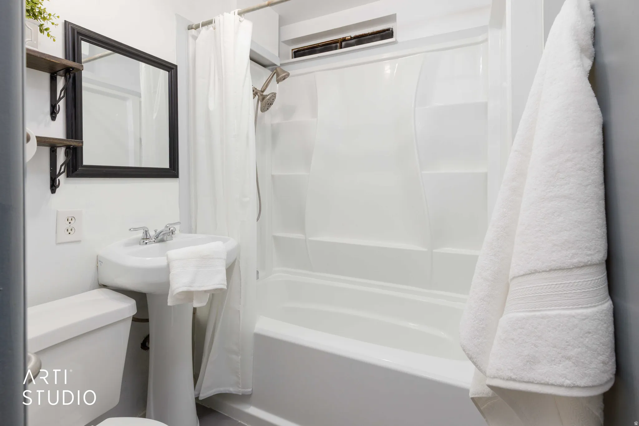 White pedestal sink with chrome faucet, a wall-mounted mirror with a black frame, and a white one-piece toilet