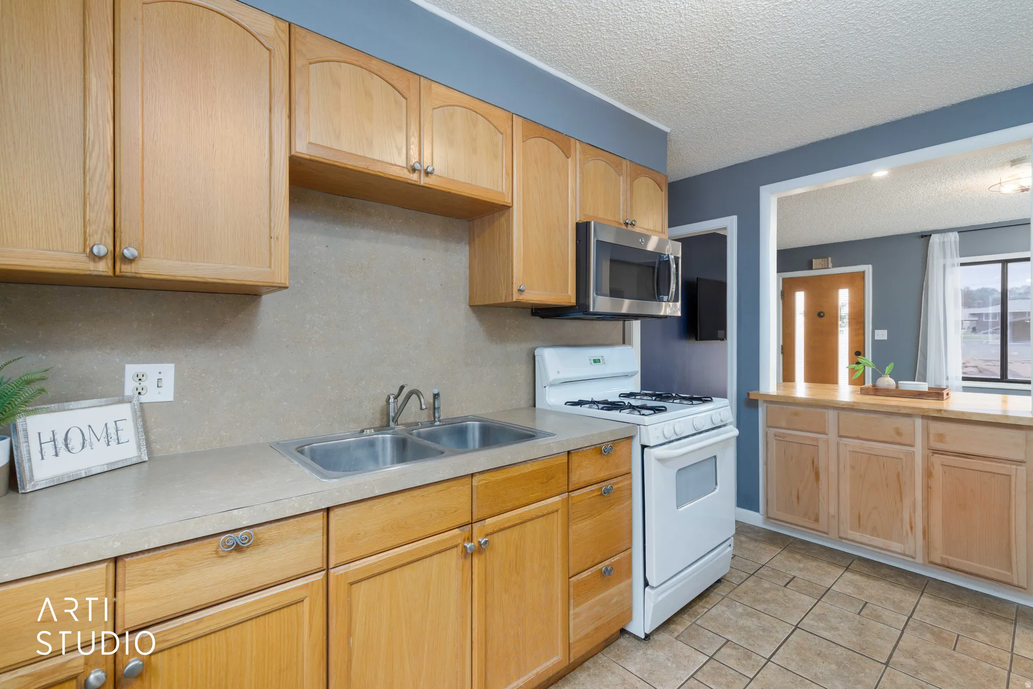 Kitchen featuring wood cabinetry, stainless steel double basin sink, and a white gas range with overhead microwave