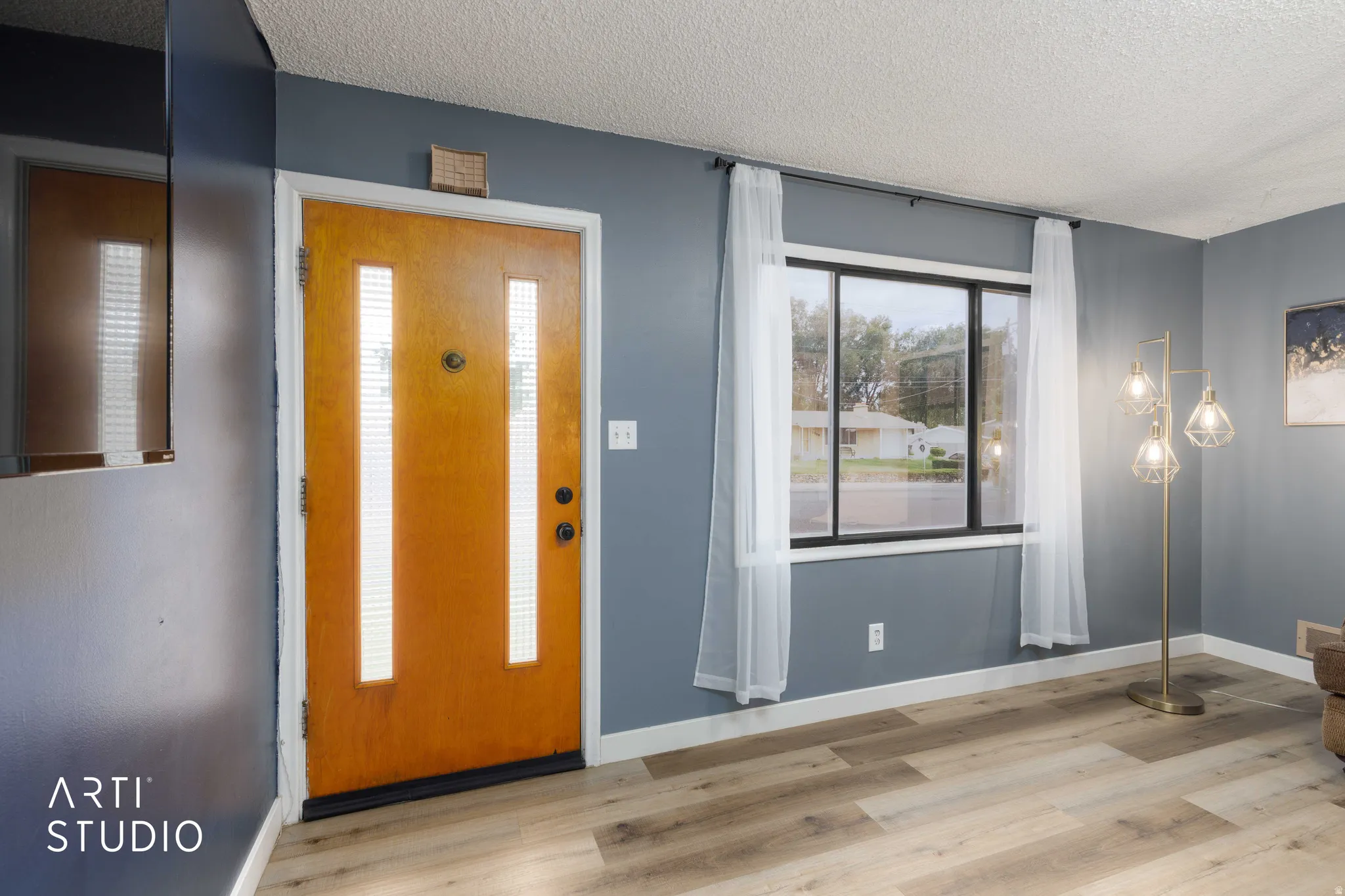 Entry area featuring a solid wood door with vertical glass inserts, contrasting gray wall paint, and light wood-finish flooring