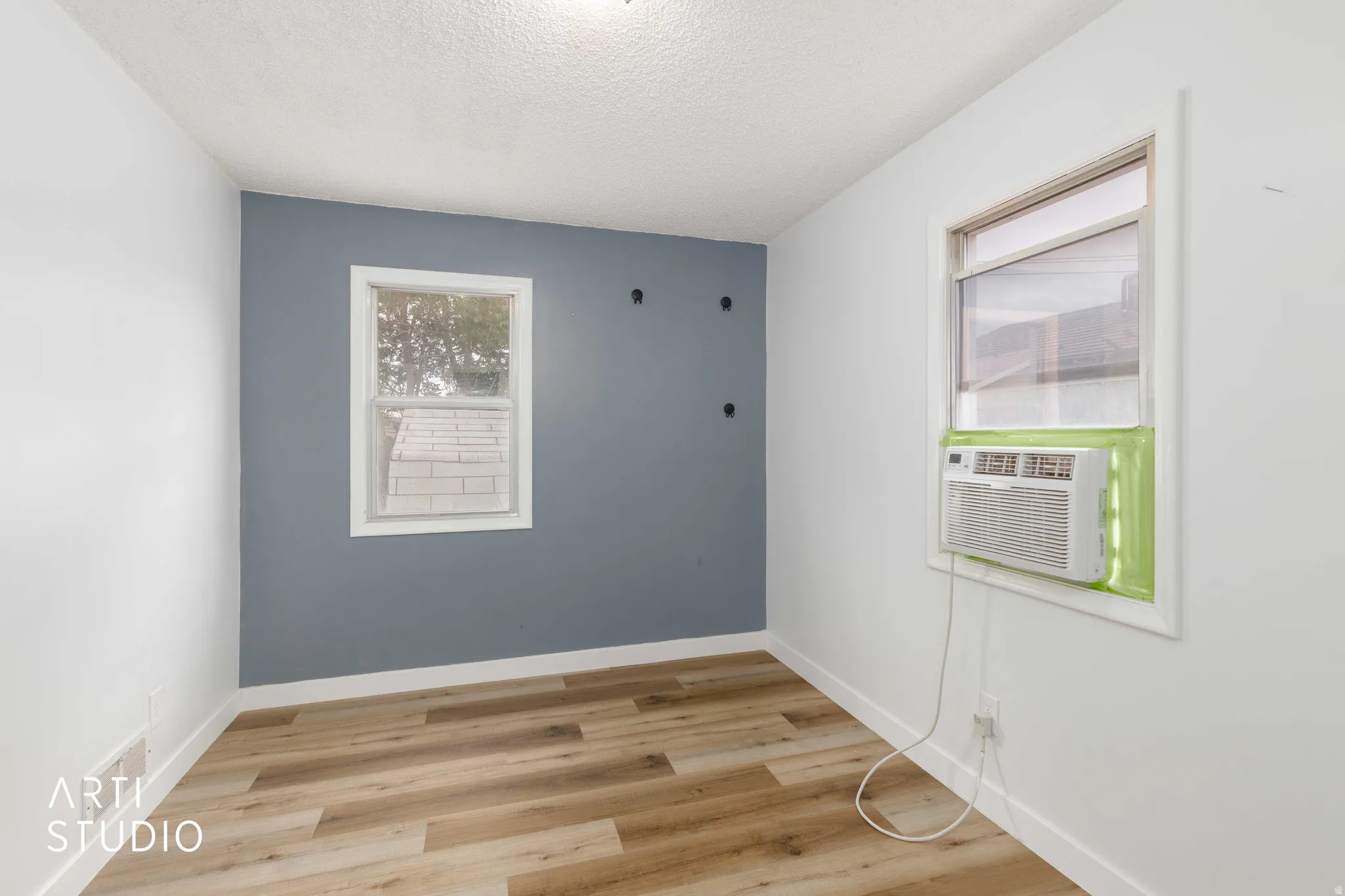 Room featuring wood-finish flooring, white baseboards, and a window with a window-mounted air conditioning unit