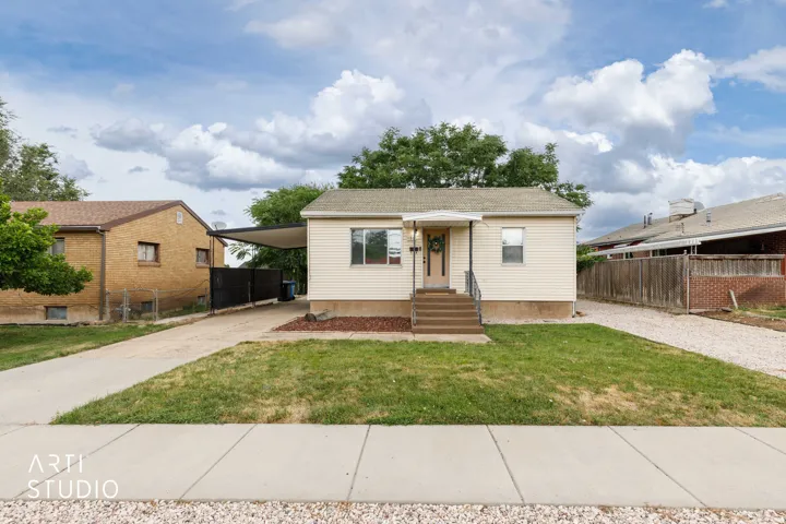 Cream-colored siding exterior with a covered front porch, concrete driveway, and a carport