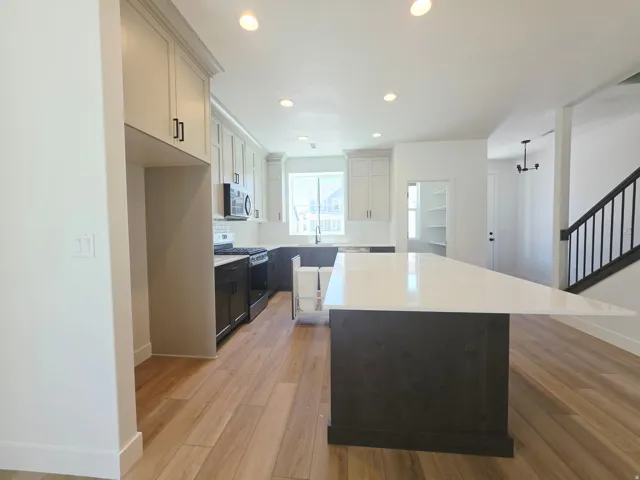 Kitchen featuring a large central island with a white countertop and dark wood-finish cabinetry, wood-finish flooring, recessed lighting, and a pantry with built-in shelving