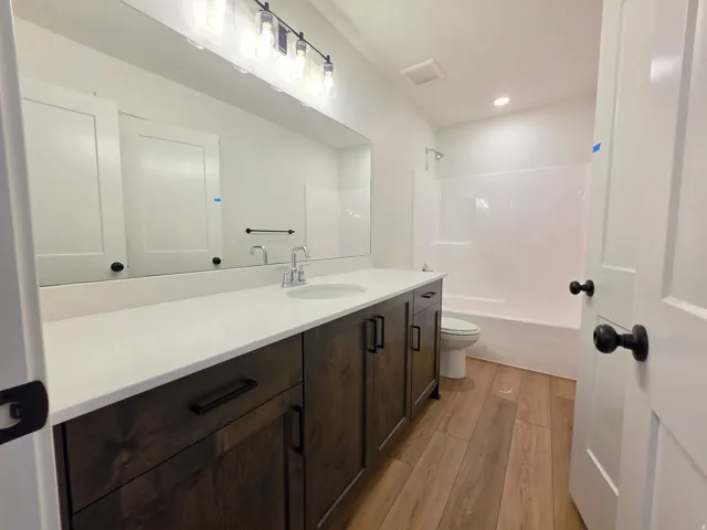 Bathroom featuring a wood-finish floor, a dark wood-finish vanity with a light-toned countertop, a rectangular undermount sink, and a built-in shower/tub combination