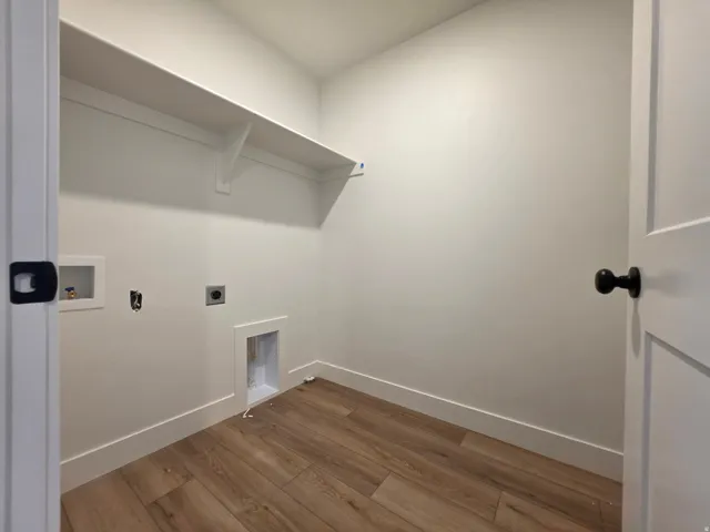 Dedicated laundry space featuring wood-finish flooring, crisp white walls, and a built-in storage shelf