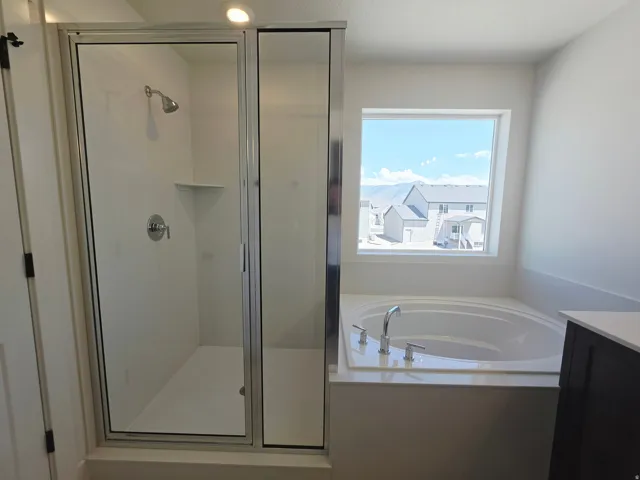 Spacious bathroom featuring a glass-enclosed shower with chrome fixtures, a built-in corner shelf, and a large soaking tub with chrome faucet