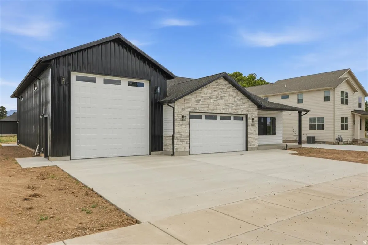 Modern residence featuring a large attached accessory building with a wide garage door, a two-car garage with a stone facade, and a concrete driveway