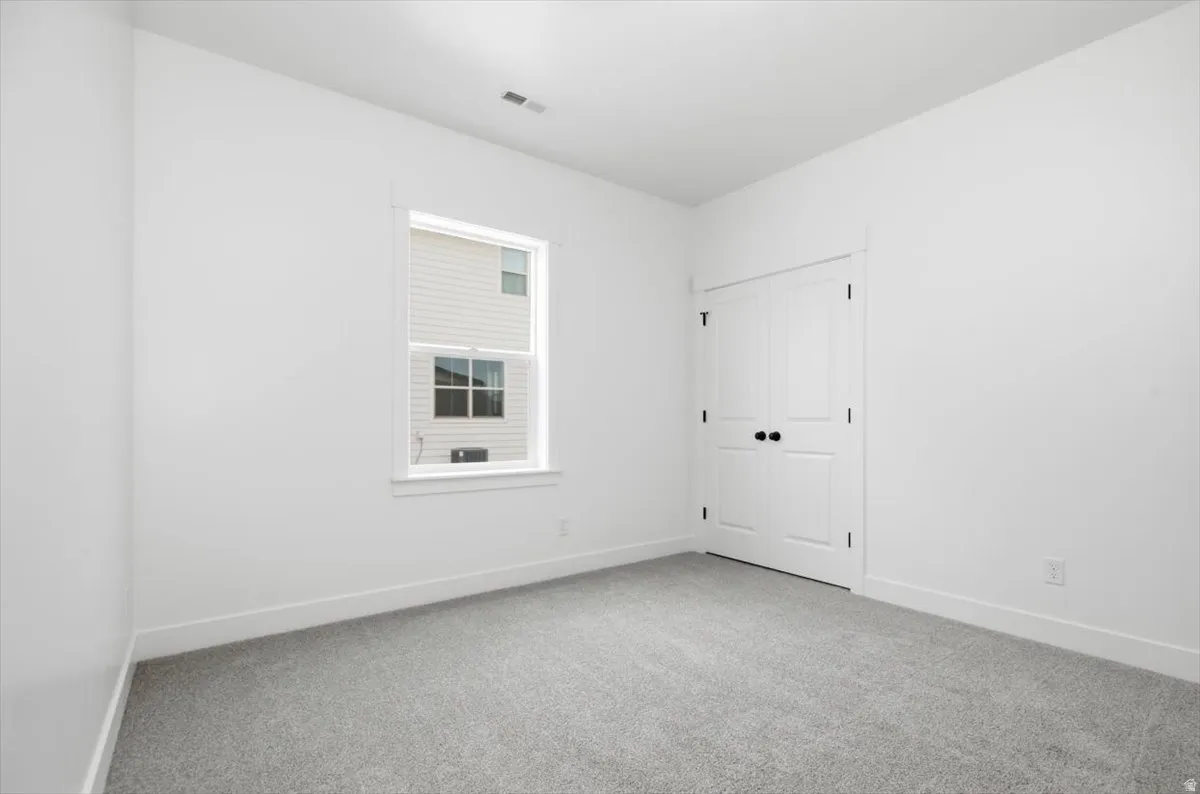 Light gray carpeted room with white walls, a single window, and white bi-fold doors with black hardware
