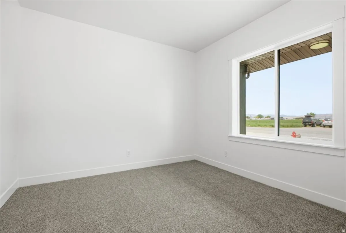 Room featuring light gray carpet flooring, white walls, white baseboards, and a large window with white trim