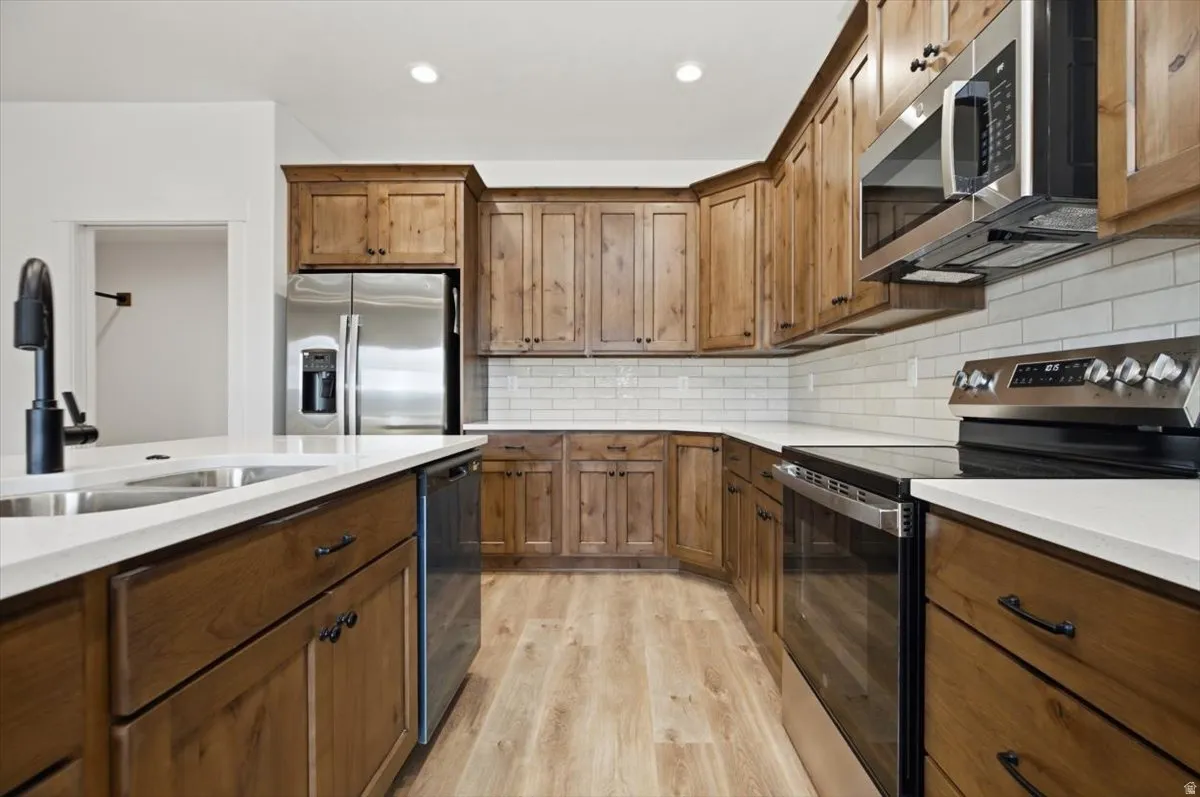 Kitchen featuring wood-finish cabinetry, stainless steel appliances, white subway tile backsplash, and light wood-finish flooring
