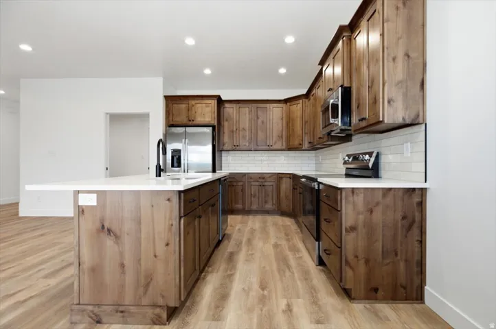 Kitchen featuring wood-finish cabinetry, stainless steel appliances, a white subway tile backsplash, and light countertops