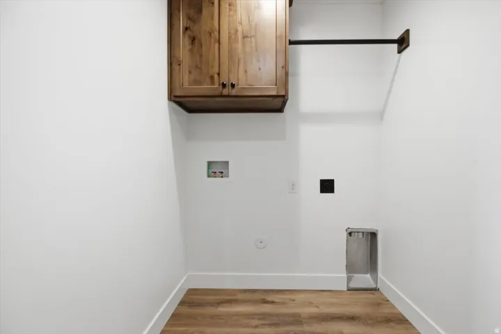 Laundry area featuring wood-finish flooring, white walls, and a built-in wood cabinet with dark hardware