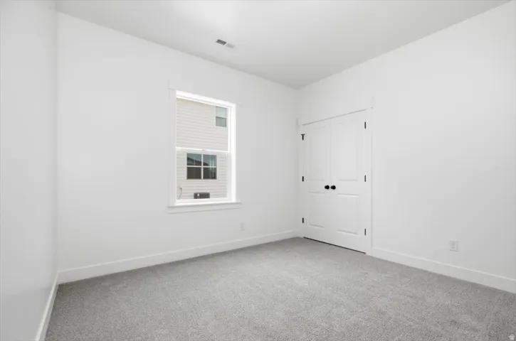 Light gray carpeted room with white walls, a single window, and white bi-fold doors with black hardware