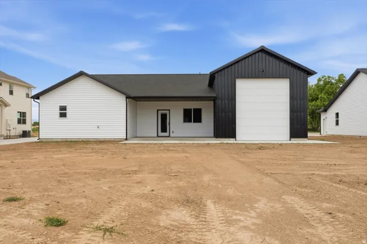Rear exterior featuring a black metal-clad workshop addition with a large white roll-up door, white vinyl siding, a dark shingle roof, and a concrete patio space