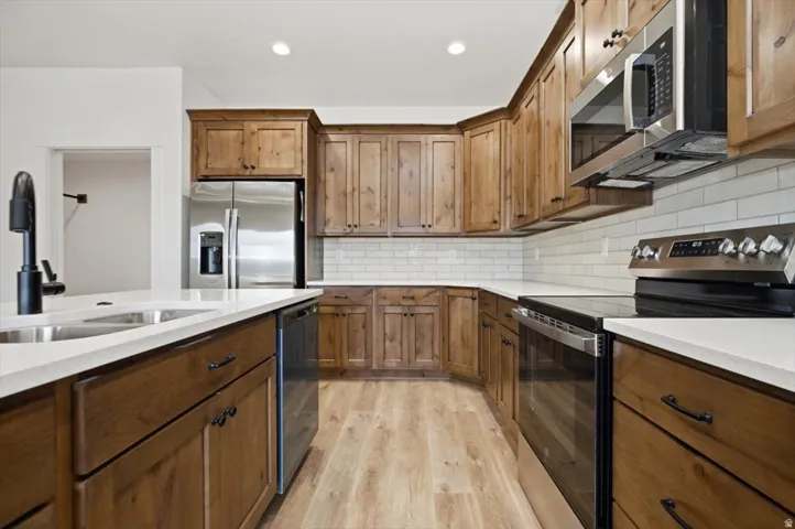 Kitchen featuring wood-finish cabinetry, stainless steel appliances, white subway tile backsplash, and light wood-finish flooring