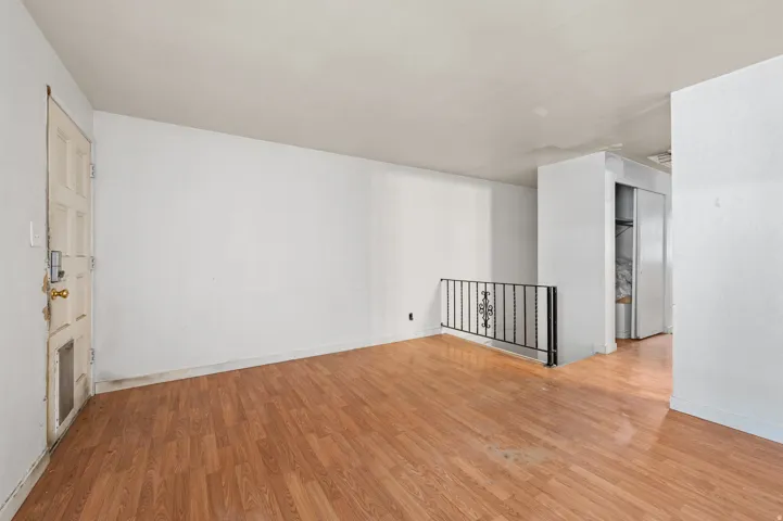 Spacious room featuring wood-finish flooring, white walls, and a black wrought iron railing