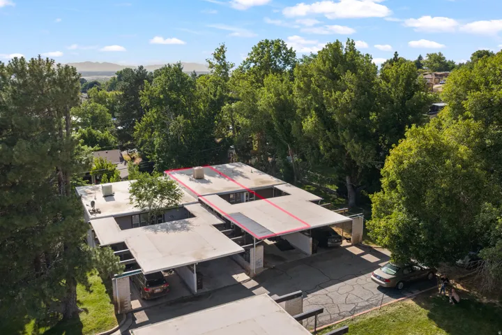 Modern architectural structure featuring multiple covered parking areas, mature perimeter trees, a flat roofline, and established landscaping